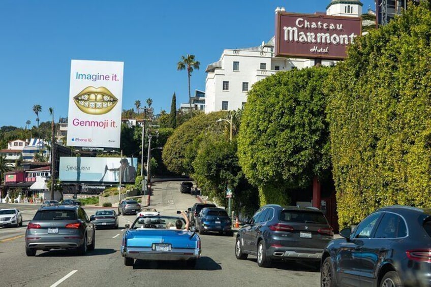 Una calle concurrida con coches, un cartel del Hotel Chateau Marmont y un anuncio de iPhone 15. 4