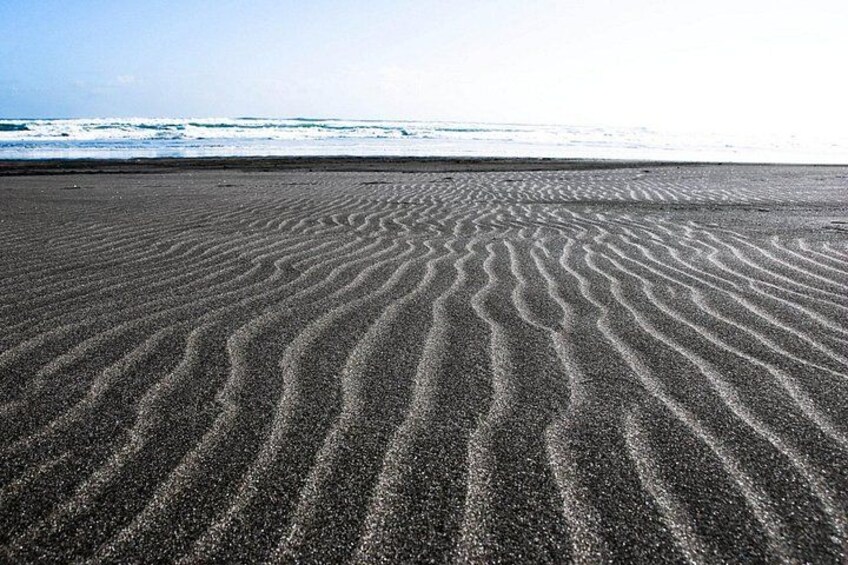 Une plage de sable avec des motifs ondulés, des vagues de l’océan en arrière-plan et un ciel dégagé. 2