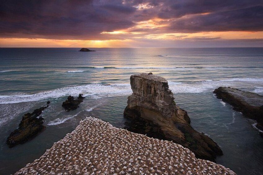 A coastal landscape with a prominent rock formation, calm sea, and a sunset. 5
