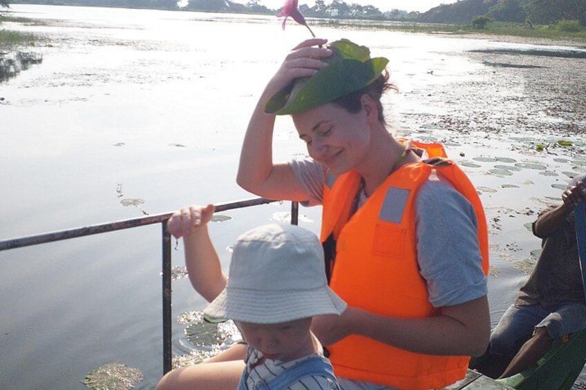 A person in a boat wearing a life jacket and a hat, with a calm river and greenery in the background. 3