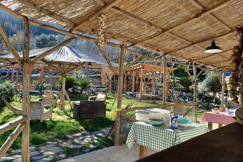 A rustic outdoor seating area with wooden tables and chairs, surrounded by greenery and a mountainous backdrop. 3