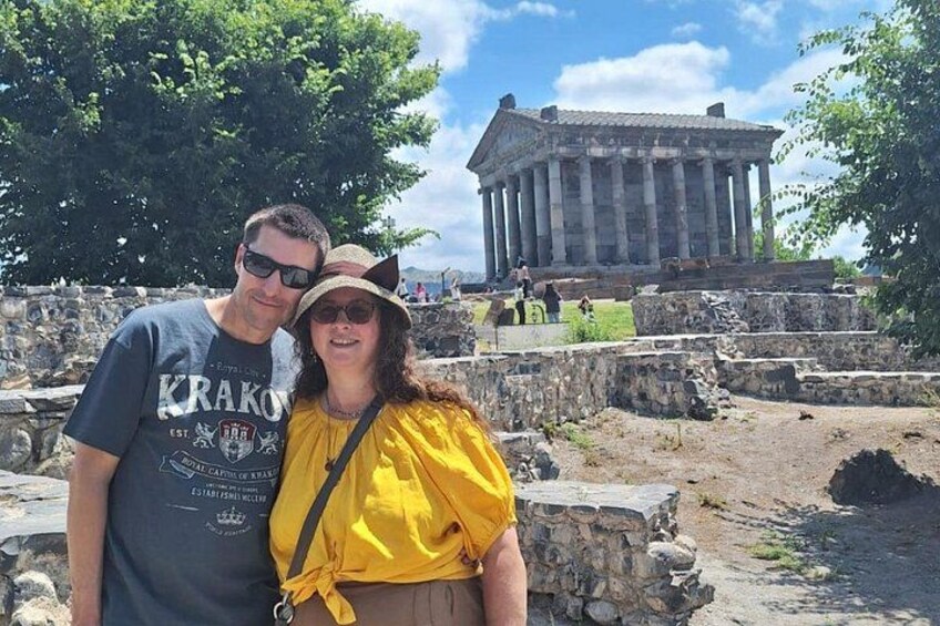 Two people standing in front of ancient ruins with columns and a large stone structure in the background. 3