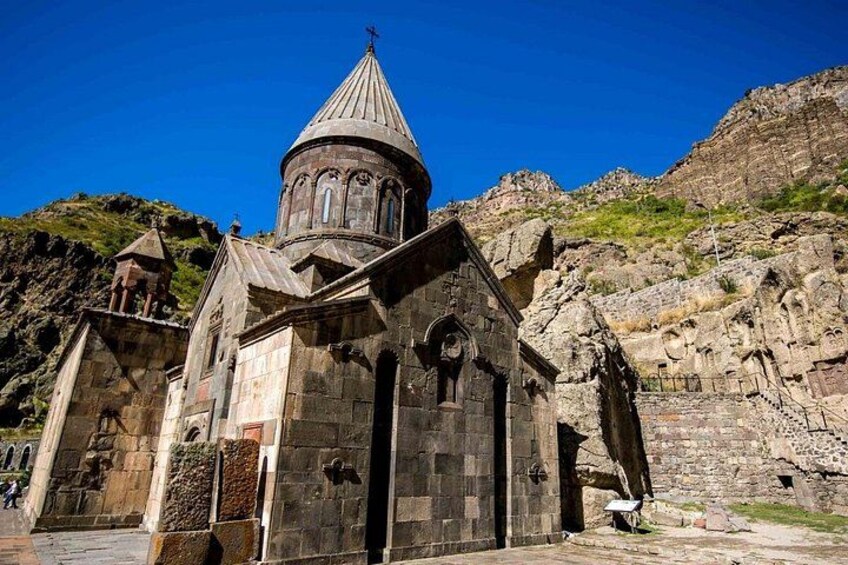 A stone church with a dome and bell tower, set against a mountainous backdrop. 2