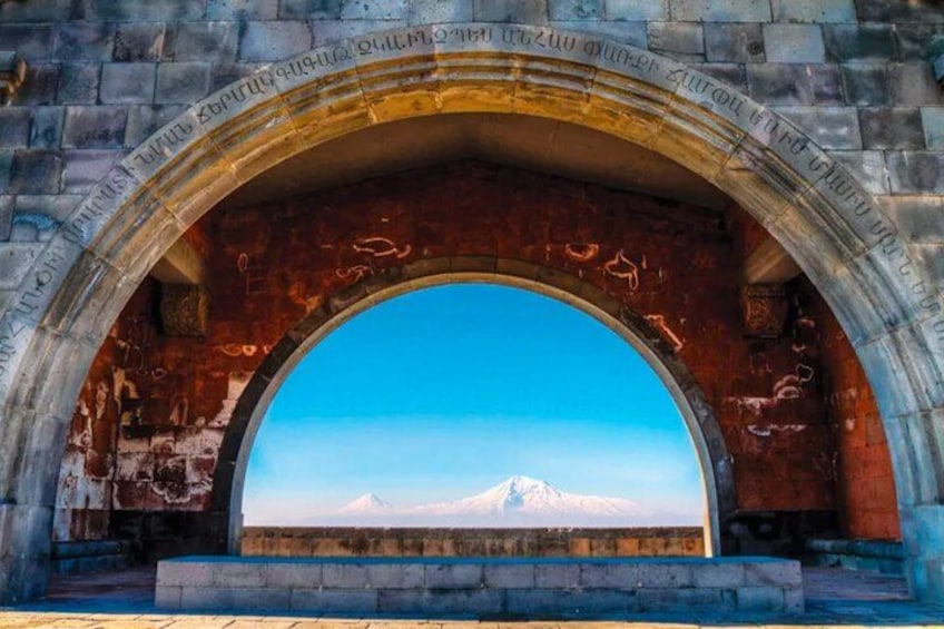An arched stone structure with inscriptions, a clear blue sky, and a distant snow-capped mountain. 4
