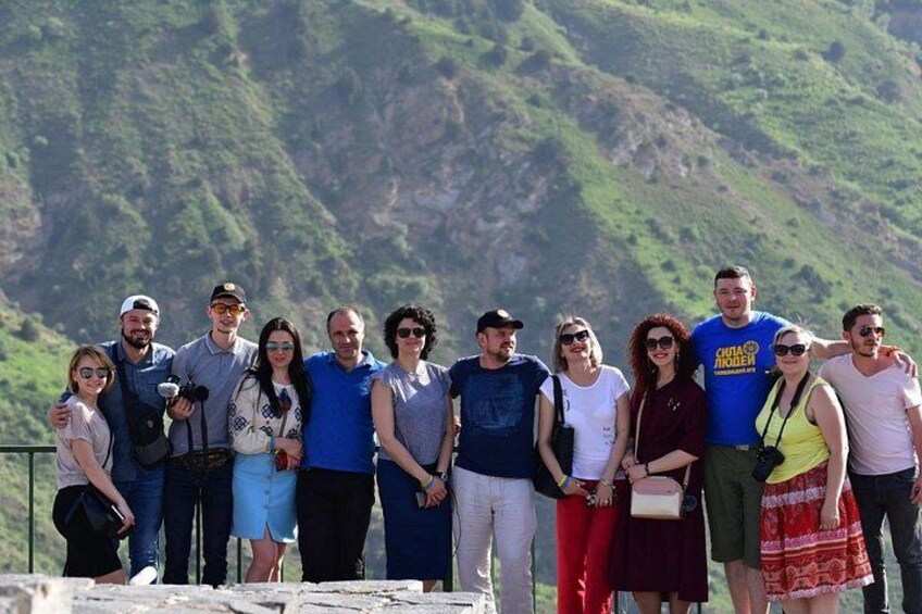 A group of people standing on a ledge with a mountainous landscape in the background. 3
