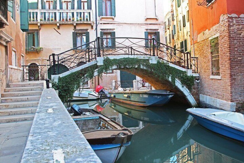 A canal with boats, a stone bridge, and buildings with balconies. 2