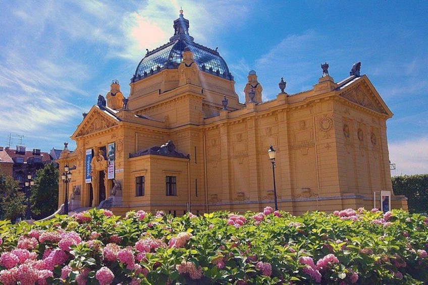 A large building with a dome and statues, surrounded by pink flowers. 1