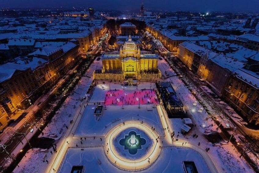 A snow-covered plaza with a central fountain, surrounded by historic buildings with illuminated facades. 3