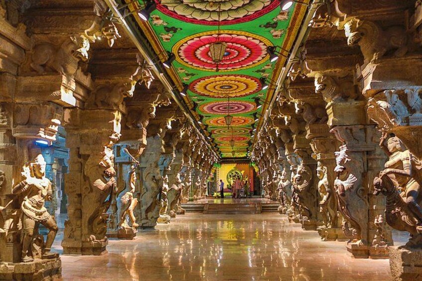 A temple corridor with ornate carvings and statues, a reflective floor, and a colorful ceiling. 5