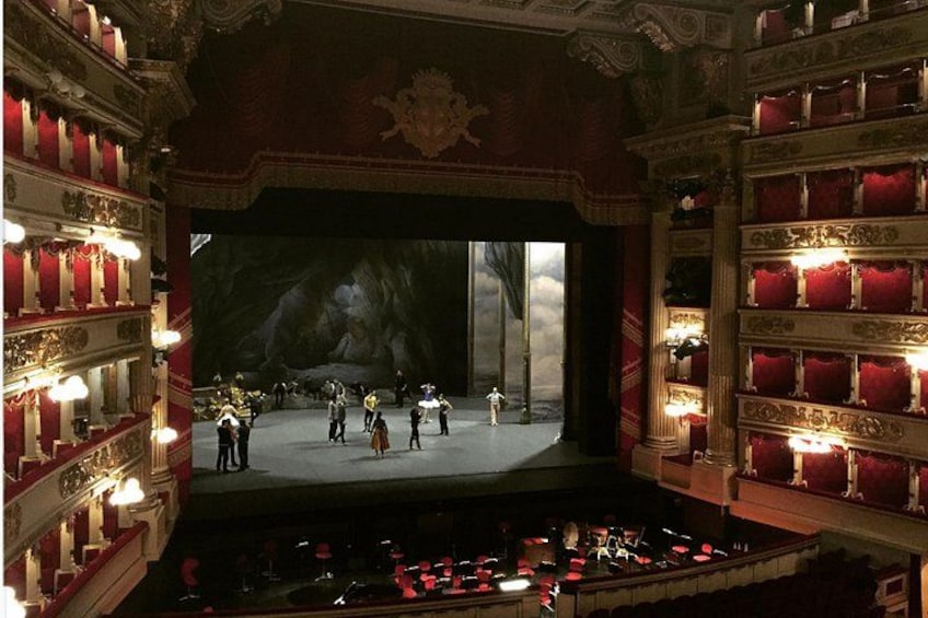 Een theater met versierde rode gordijnen, een podium en een balkon met rode zitplaatsen. 1