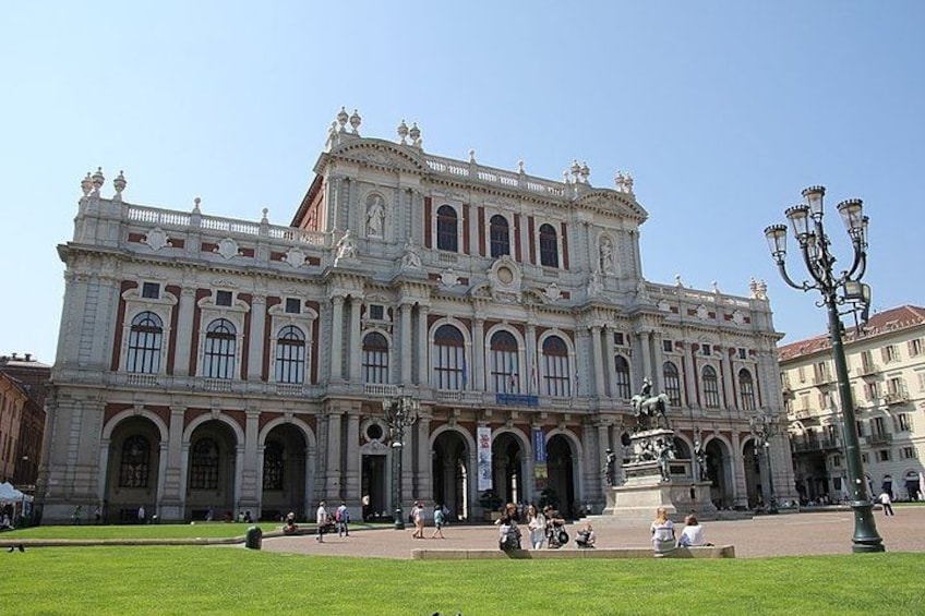 A large historic building with ornate architecture, a central statue, and a well-maintained lawn in front. 2
