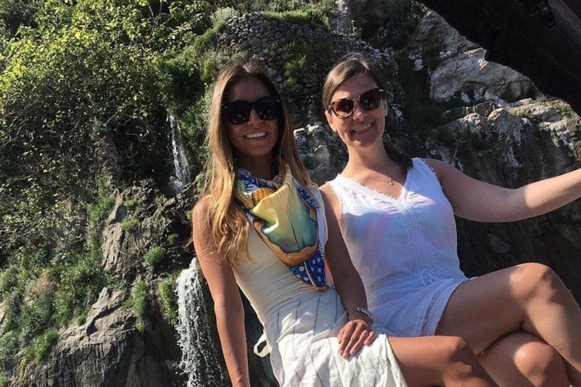 Two people sitting on a rocky outcrop with greenery in the background. 1