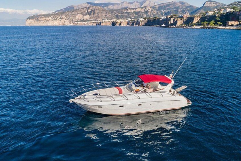 A white yacht with a red canopy on a calm sea, with a coastal town and mountains in the background. 4