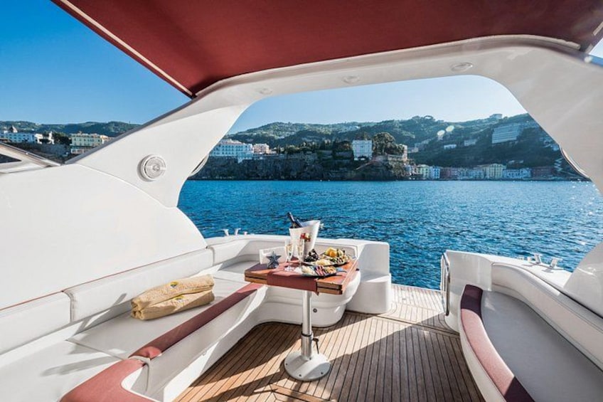 A boat deck with a table set for dining, a cushioned seating area, and a view of a coastal town across the water. 2