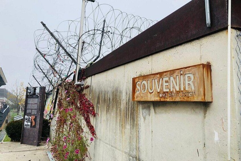 A wall with a sign that reads 'SOUVENIR' and a barbed wire fence above it. 3