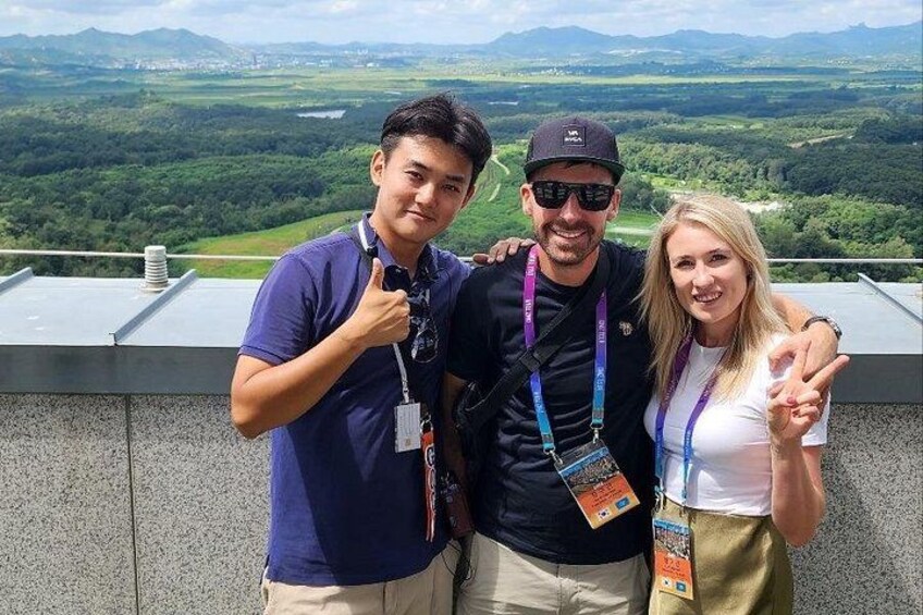 Three people standing on a rooftop with a scenic view of a valley and mountains in the background. 5