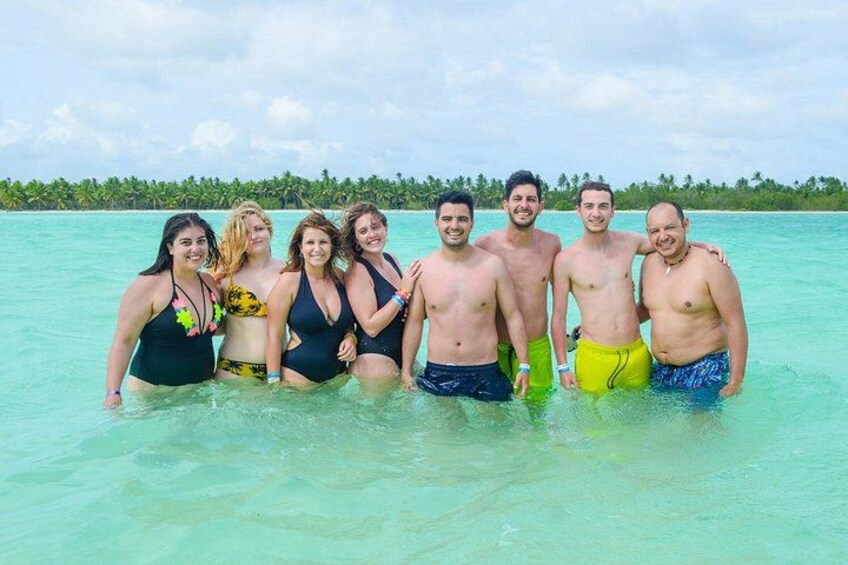 Eine Gruppe von Menschen im seichten, türkisblauen Meer, bewölkter Himmel und eine Reihe von Palmen im Hintergrund. 4