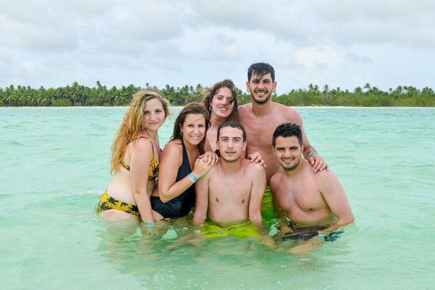 Eine Gruppe von Menschen in einer tropischen Umgebung mit klarem türkisblauem Wasser und einer Reihe von Palmen im Hintergrund. 3