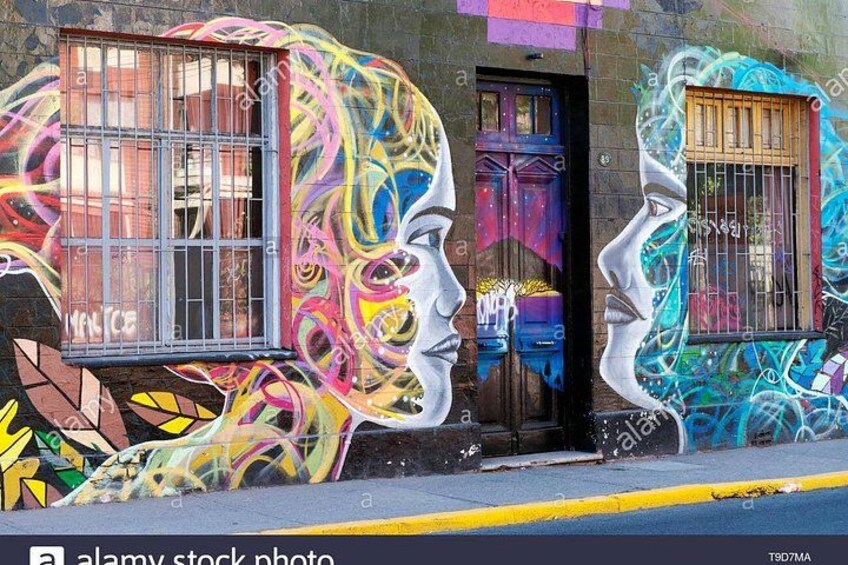 A street with colorful graffiti on a building, including a large mural of two faces. 4