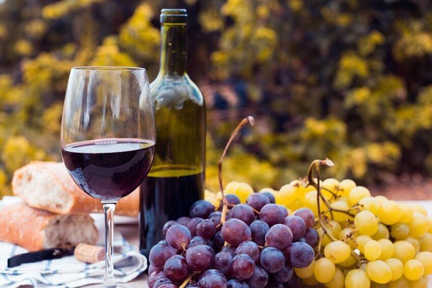 A wine glass, a bottle, and bunches of grapes on a table. 5