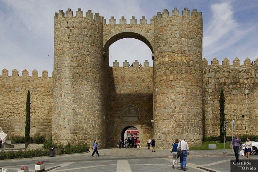 A historic stone gate with a large archway, surrounded by stone walls and towers. 1