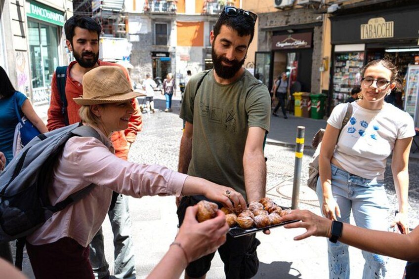 Une scène de rue où l’on voit des gens manger, un magasin avec une enseigne indiquant « TABACCHI », et un bâtiment avec une enseigne « MANCHEVALLO ». 3