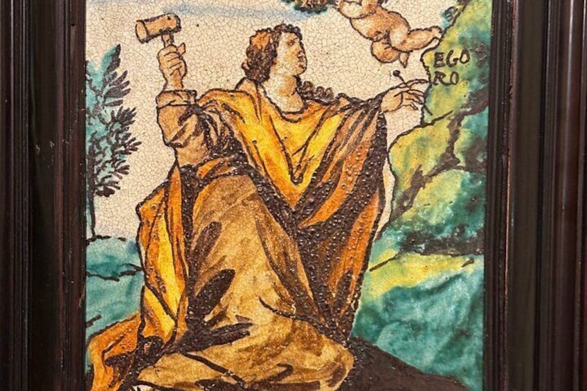 A mosaic with a figure holding a hammer, surrounded by foliage and a landscape. 4