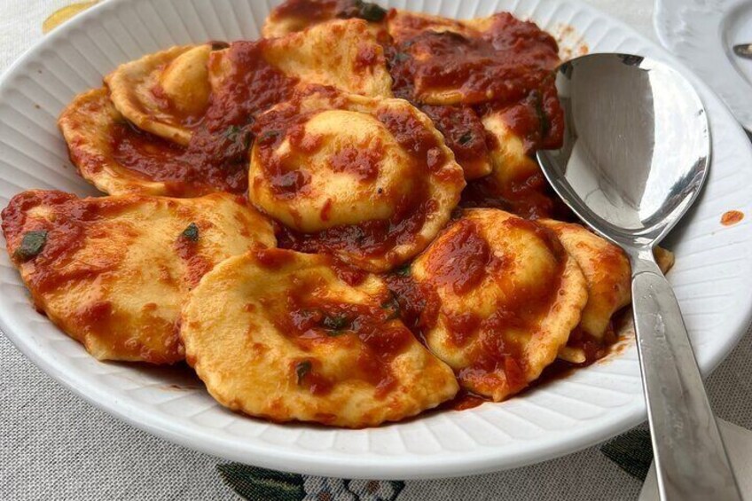A plate of ravioli with tomato sauce and herbs. 1