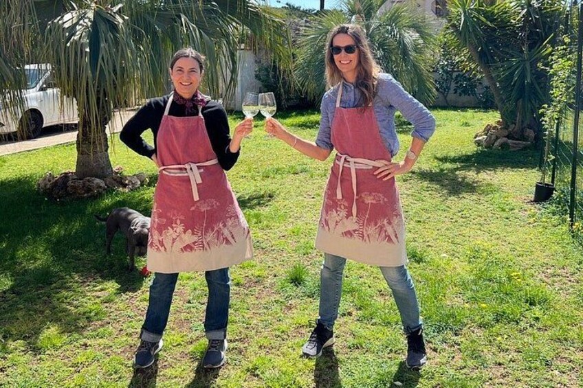 Dos personas con delantales de pie sobre césped, con un perro y palmeras al fondo. 2