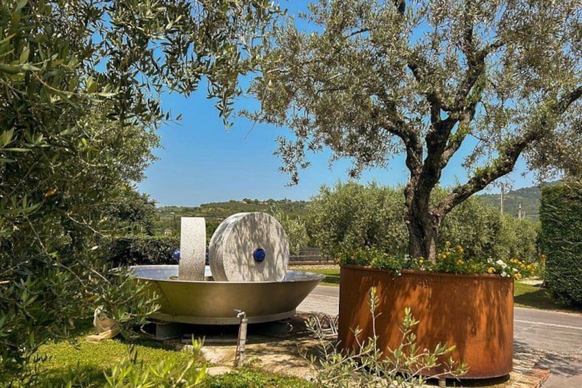A garden with a large metal sculpture, a tree, and a metal barrel. 2
