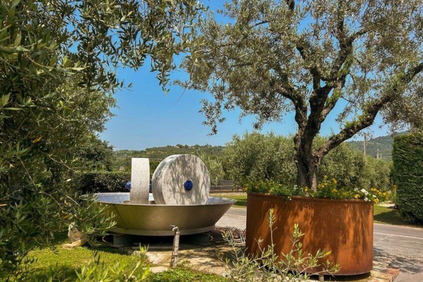 A garden with a large metal sculpture, a tree, and a metal barrel. 2