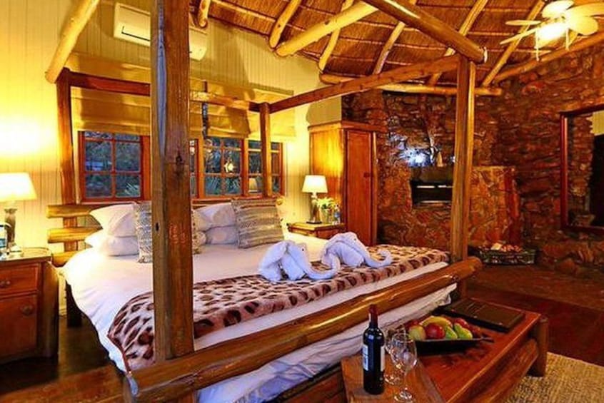 A wooden four-poster bed with white linens and towels, a stone fireplace, and a wooden nightstand with a bottle and glass. 2