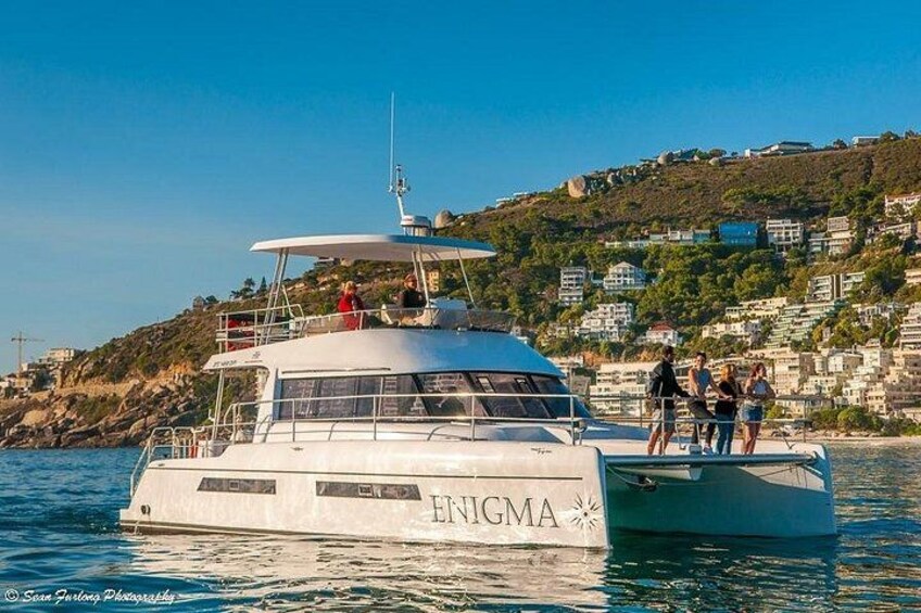 Eine weiße Yacht namens ENIGMA auf ruhigem Wasser, im Hintergrund eine Küstenstadt. 1