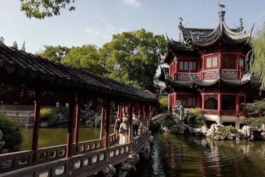Un pabellón chino tradicional junto a una masa de agua tranquila, un puente de madera y un edificio rojo de varios niveles. 1
