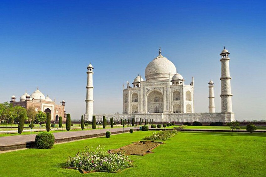 The Taj Mahal, a large white marble mausoleum with four minarets, surrounded by well-manicured gardens and pathways. 1