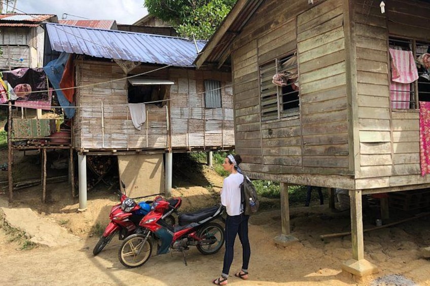 A wooden house with a motorcycle parked in front, a person standing nearby, and a dirt path. 4
