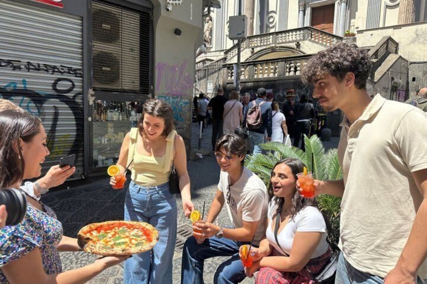 Un gruppo di persone all'aperto, alcune con bevande e una con una pizza. 1