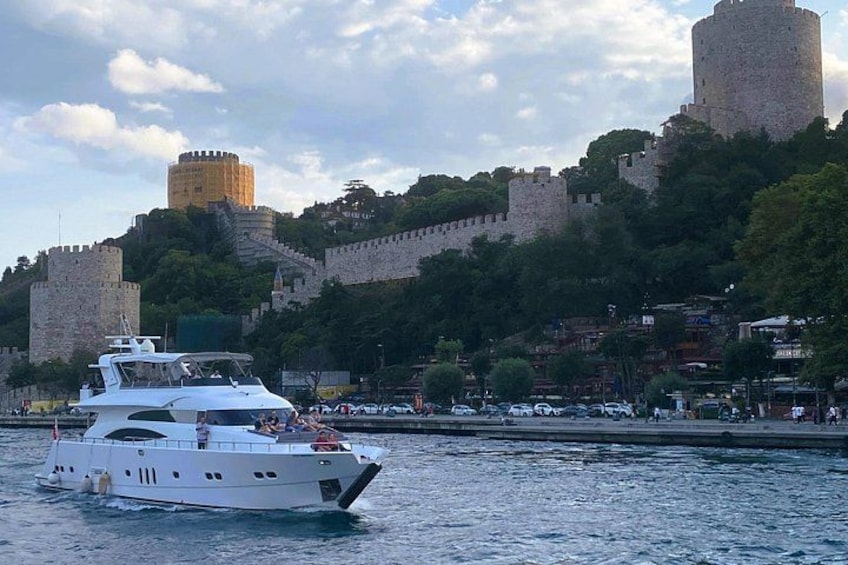 A white yacht on calm water, a historic castle on a hill, and a cityscape with buildings in the background. 2