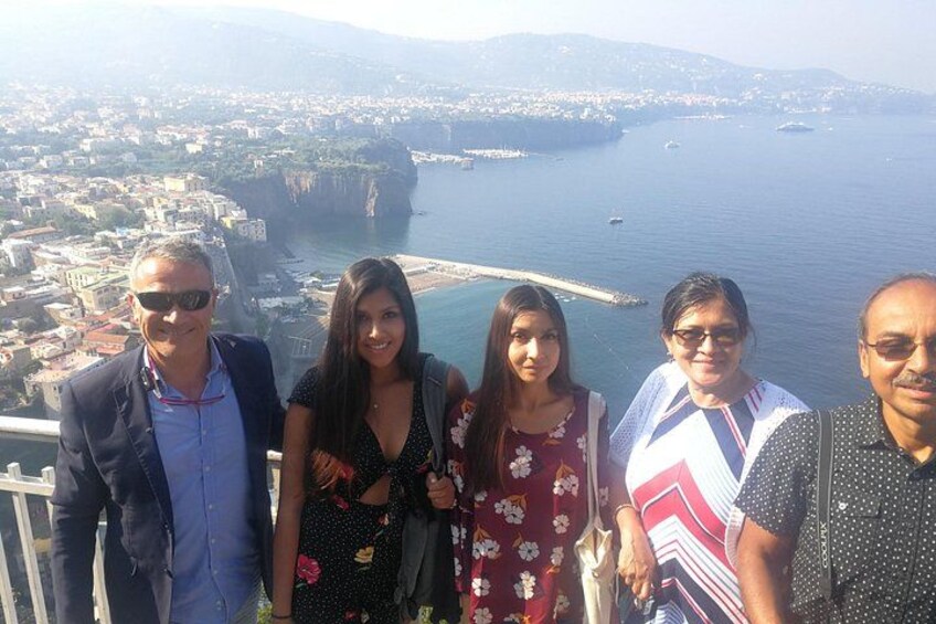A group of people standing on a balcony overlooking a coastal city with a prominent cliff and a body of water. 2