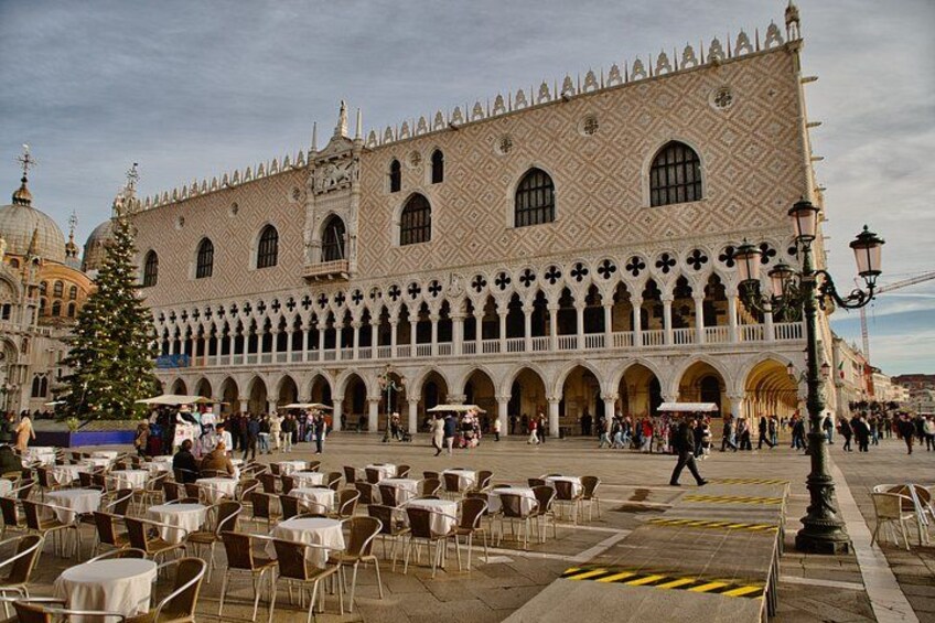 A historic building with a patterned facade and arched windows, surrounded by outdoor seating areas and a Christmas tree. 4