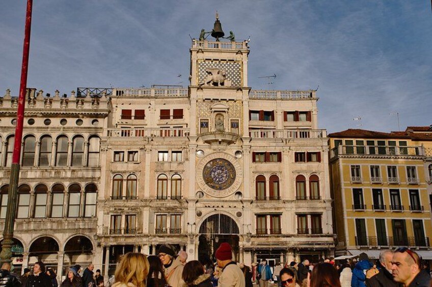 A historic building with a clock tower, arched windows, and a crowd of people in front. 3