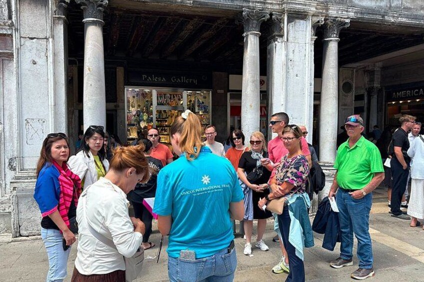 A group of people standing in front of a building with columns, a sign reading 'Palace Gallery,' and a shop with various items on display. 5