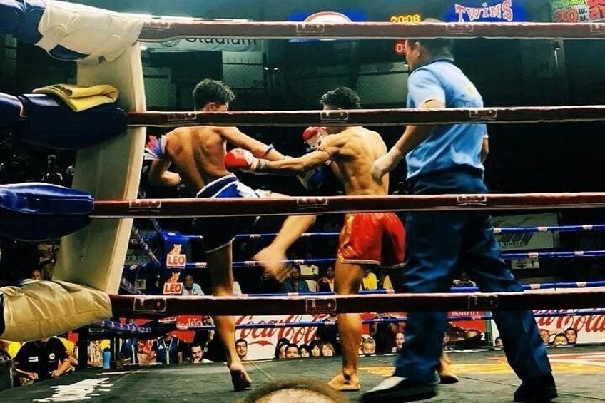 A boxing ring with two fighters, a referee, and a crowd in the background. 3