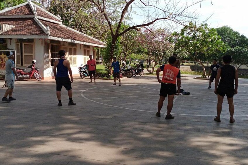 A group of people playing basketball on an outdoor court, with trees and a building in the background. 3