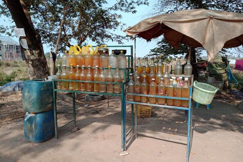 A makeshift outdoor market stall with various glass bottles and containers, a blue metal frame, and a green plastic basket. 4