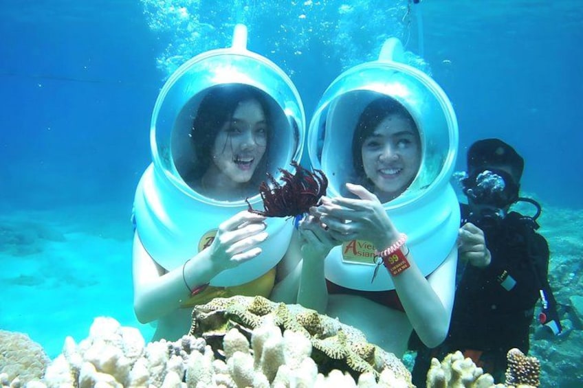 Two people underwater wearing diving helmets, surrounded by coral. 2