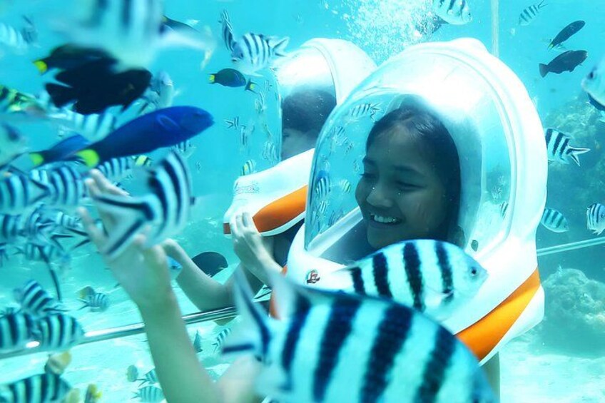 A person in a transparent helmet underwater, surrounded by fish. 2