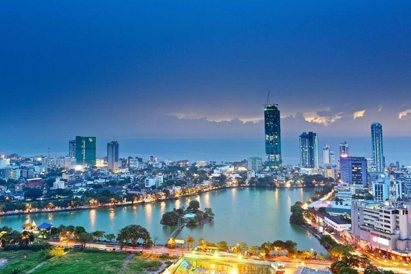 A cityscape at dusk with illuminated buildings, a river, and a bridge. 1