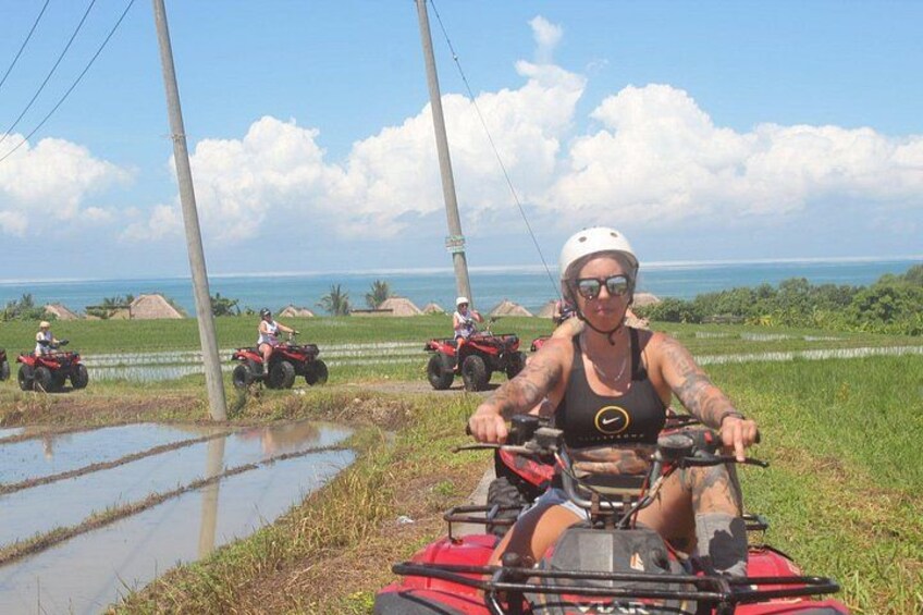 Una persona guida un quad rosso su una strada di campagna, sullo sfondo si vedono campi e una distesa d'acqua. 5