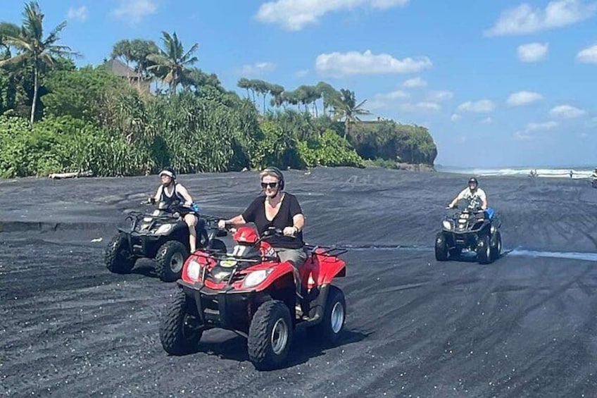 Trois personnes conduisent des quads sur une plage de sable noir, avec des palmiers en arrière-plan. 4